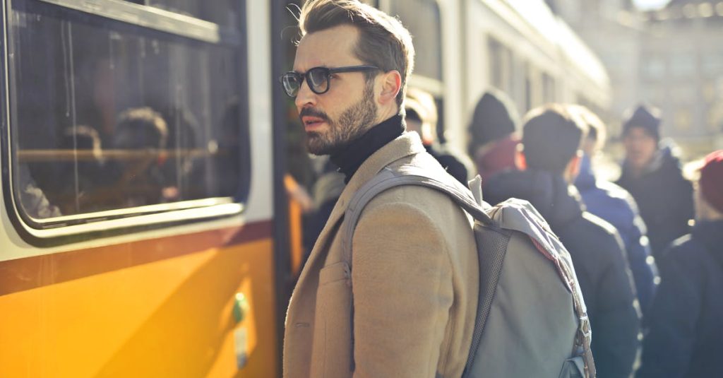A stylish man with a backpack boards a tram in bustling Budapest, Hungary, during the day.